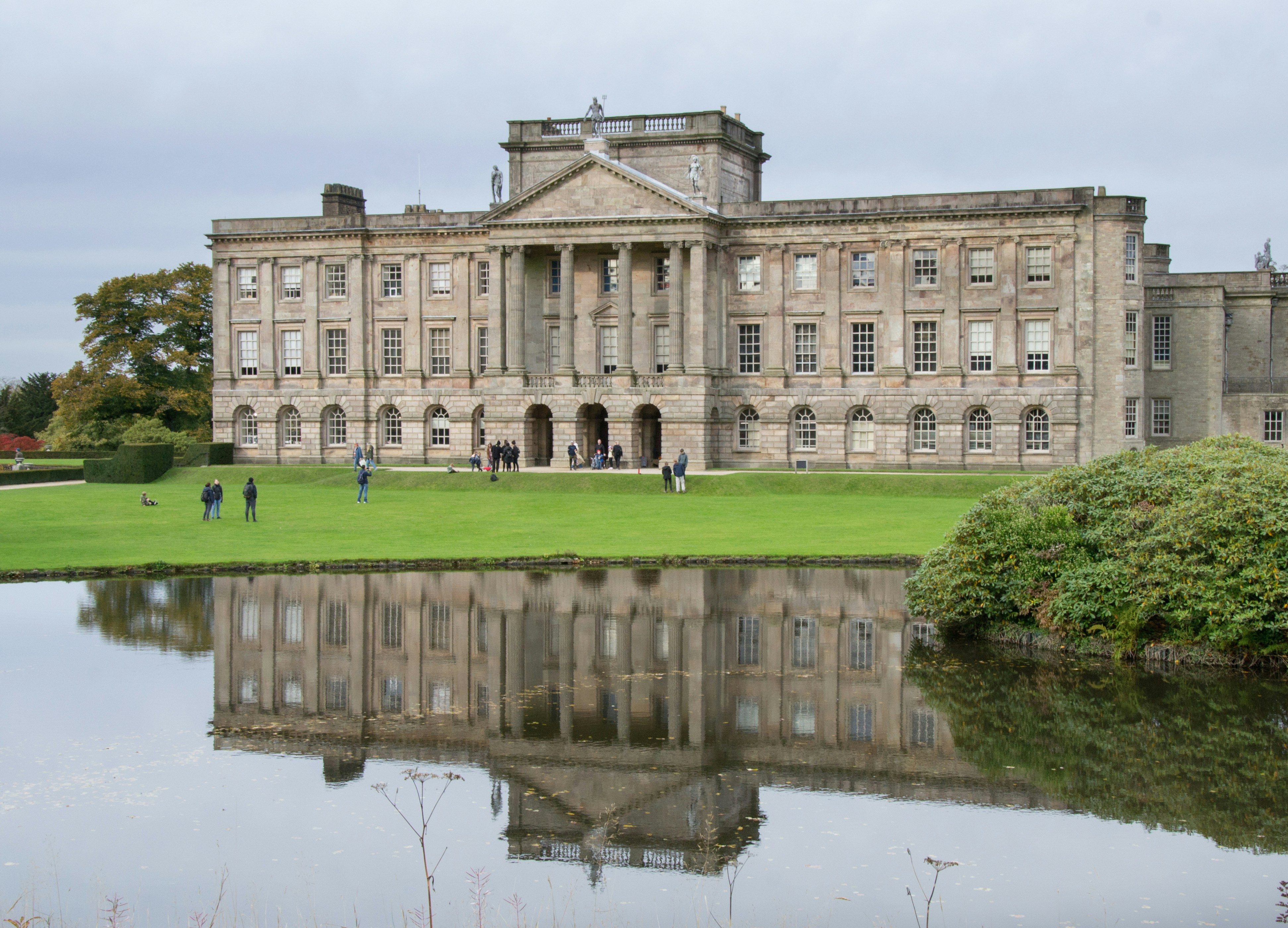 Grand heritage country house reflected in ornamental lake, showing significant Palladian architecture