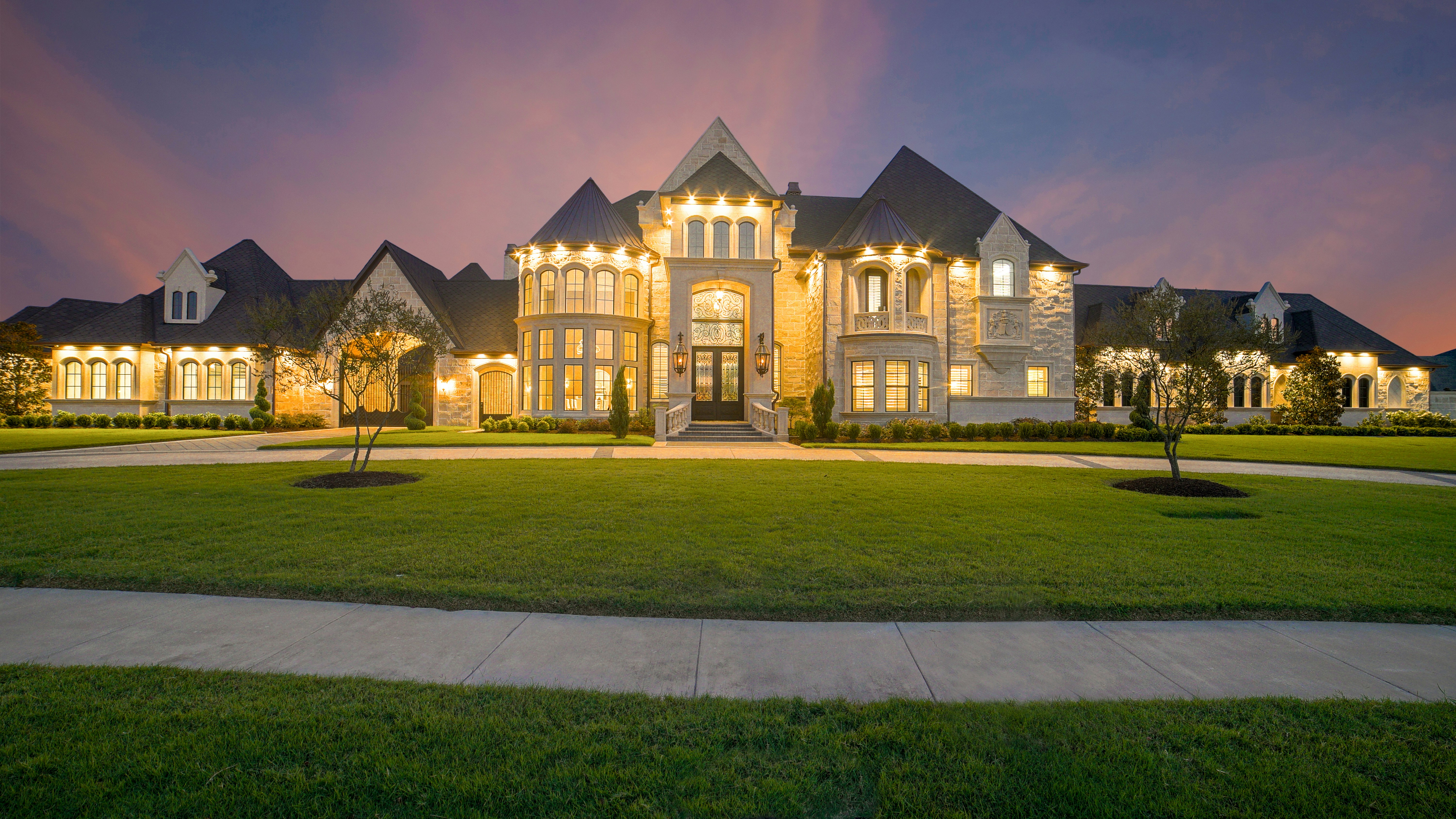 Significant private estate illuminated at dusk with stone facade and manicured grounds